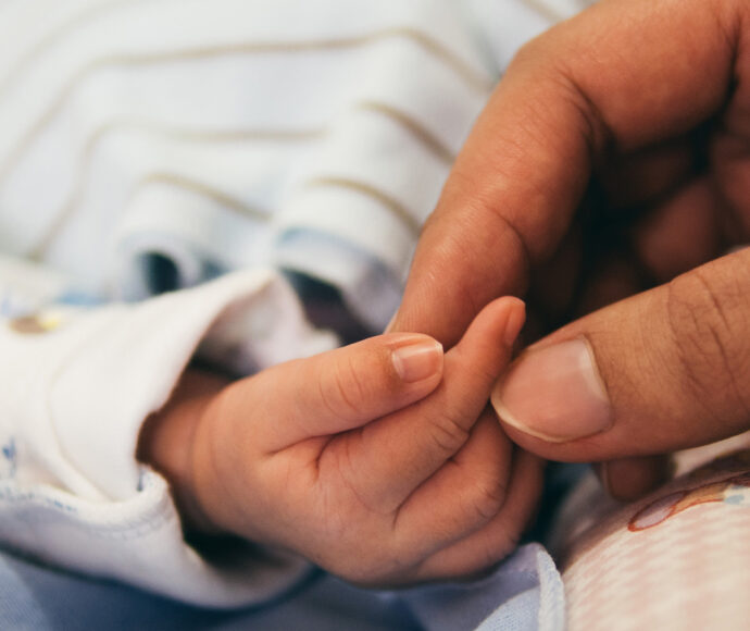 Womans hand holding an infants hand.