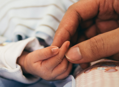 Womans hand holding an infants hand.