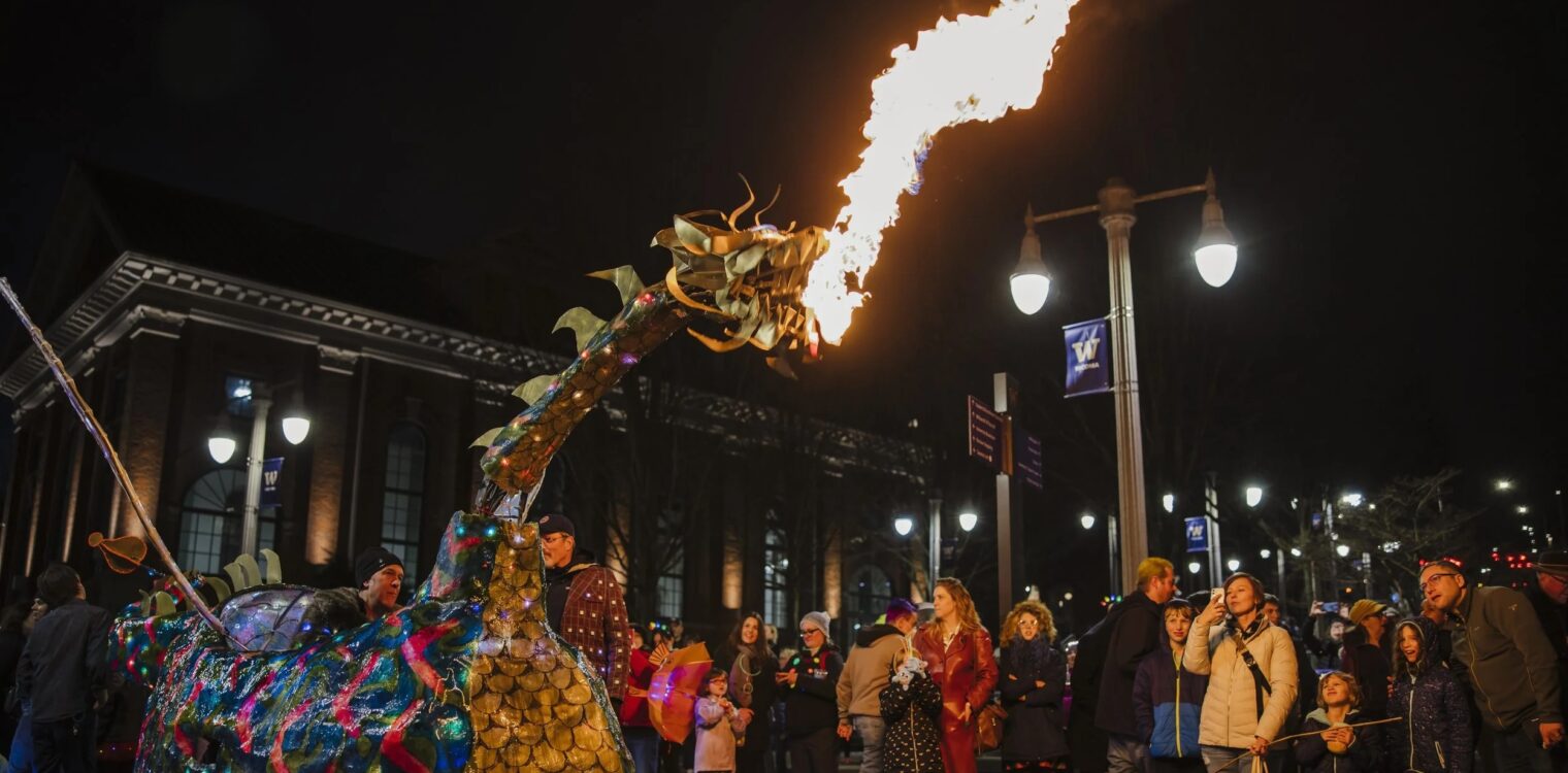 Parade crowd looks on at a fire breathing dragon parade float at Tacoma Light Trail at nighttime.