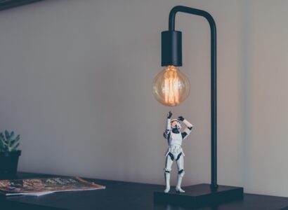 A storm trooper figurine looking up under a lit edison bulb.