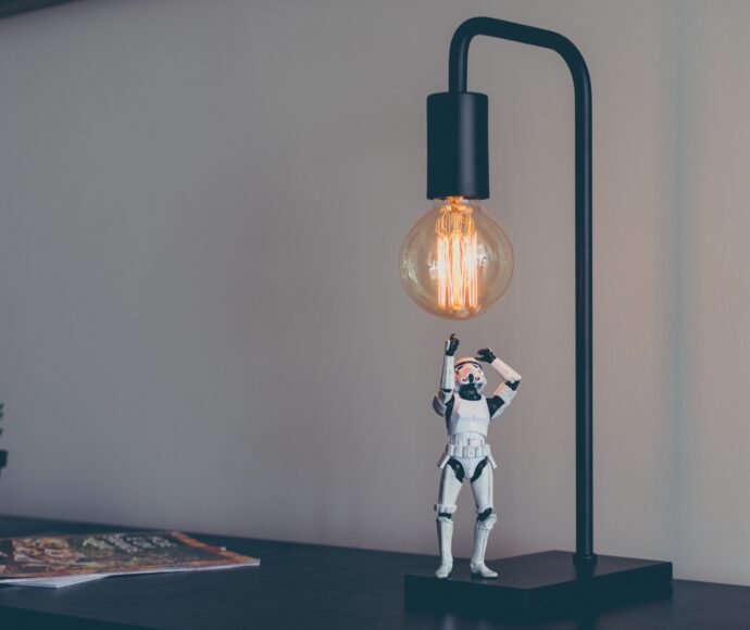 A storm trooper figurine looking up under a lit edison bulb.