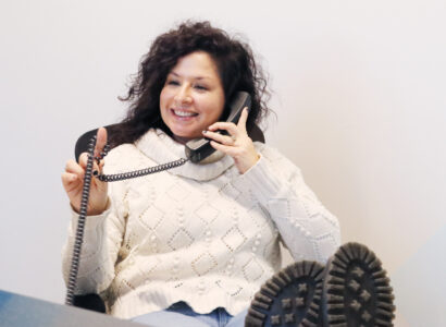 SiteCrafting employee Jen Rittenhouse holding a phone to her ear with her feet propped up on desk.