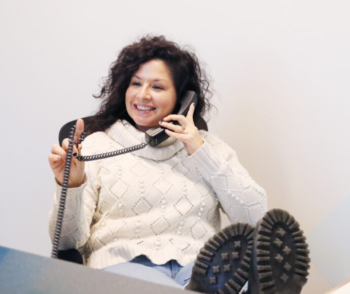 SiteCrafting employee Jen Rittenhouse holding a phone to her ear with her feet propped up on desk.