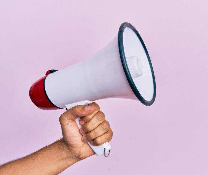 Hand holding a megaphone on a pink background