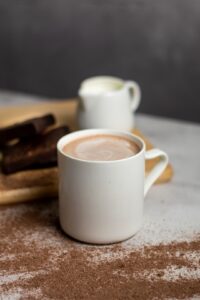 Simple mug of hot chocolate on table with ground cocoa and a small creamer pitcher