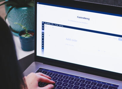 Person sitting at a laptop, with Wordpress Gutenberg page editor on the screen.