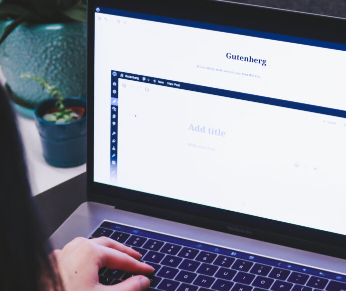 Person sitting at a laptop, with Wordpress Gutenberg page editor on the screen.