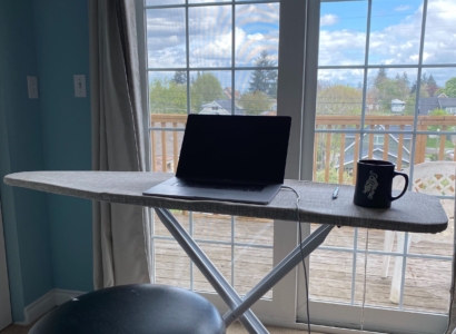 Laptop and coffee cup on an iron board in front of a sliding glass door.