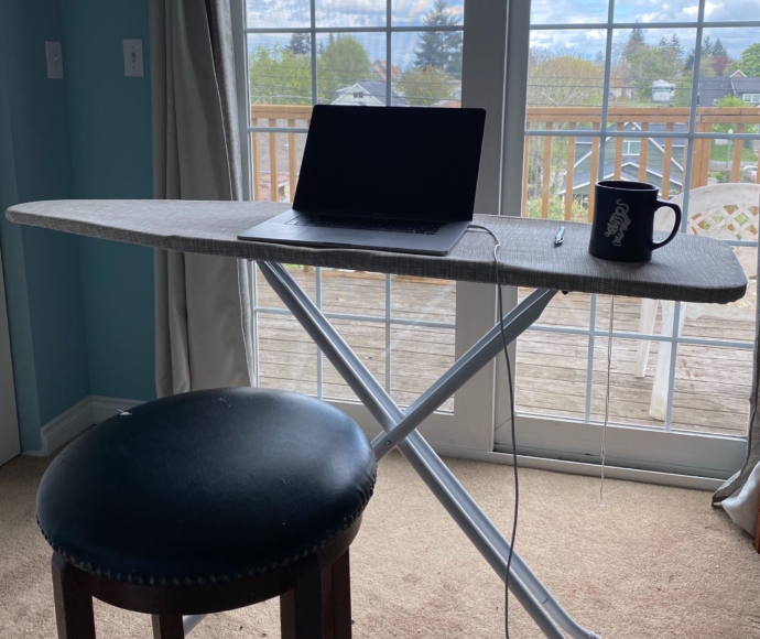 Laptop and coffee cup on an iron board in front of a sliding glass door.