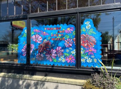 Store window painted with flowers and the phrase Friends are everywhere