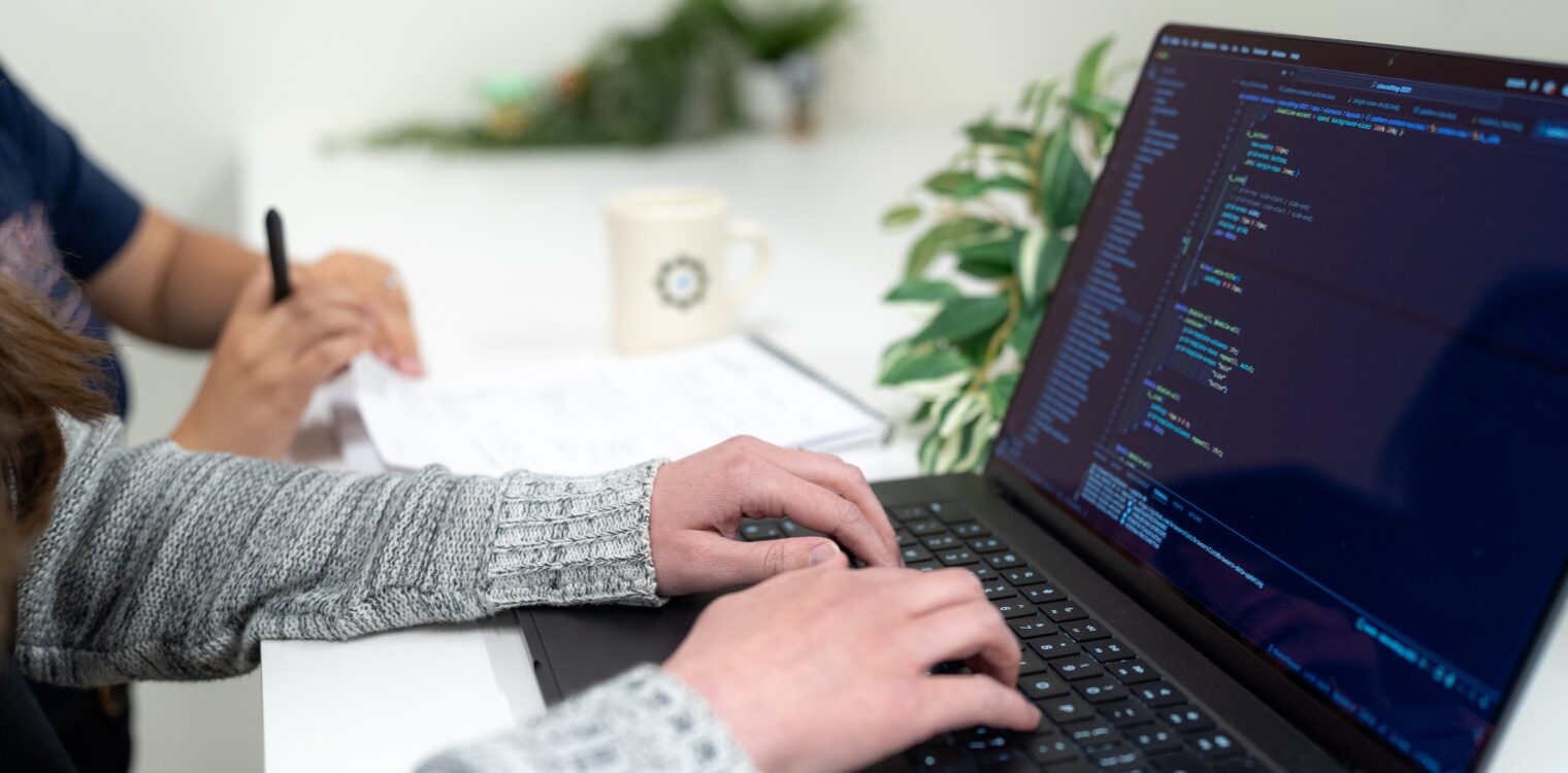 Hands typing on a laptop keyboard writing code.