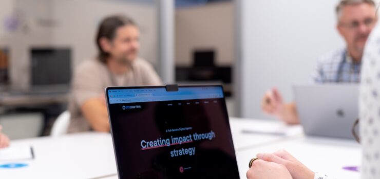 Employees in conference room looking at laptop.