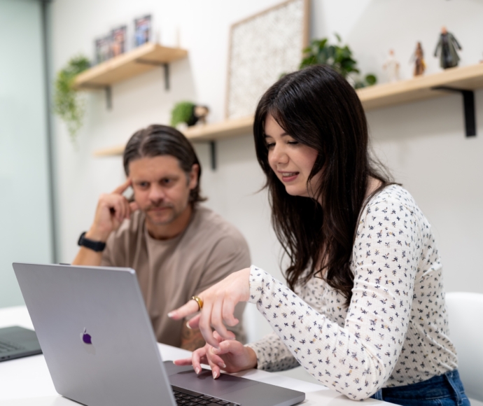 Employee pointing to laptop screen with fellow employee looking over
