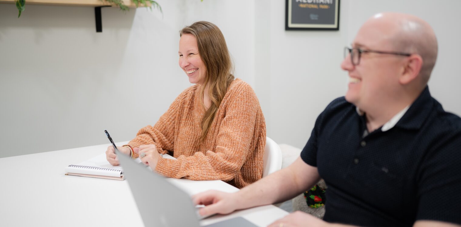 Two employees smiling while working together in a conference room.