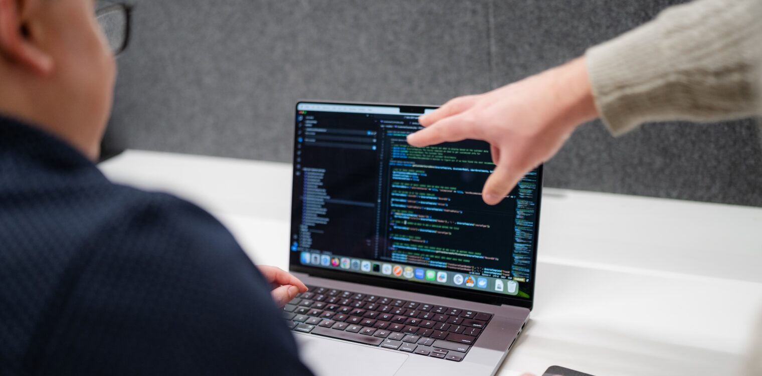 Employees discussing code on a laptop.