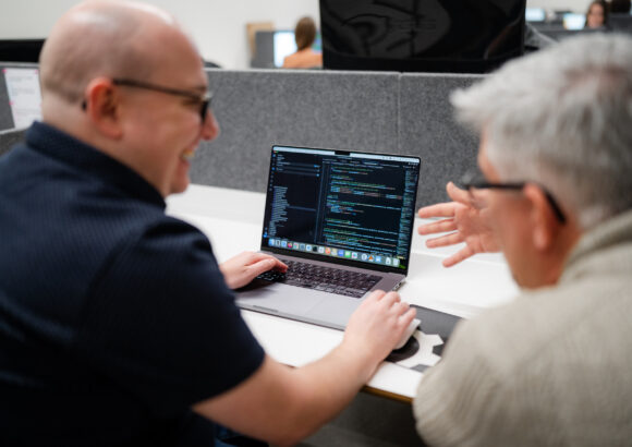 Smiling coworkers looking at code on a laptop.