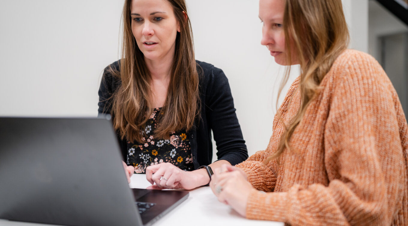 Two employees looking at code on a laptop