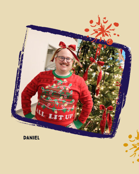 SiteCrafting employee Daniel wearing a red sweater with different color Christmas lights that reads, 