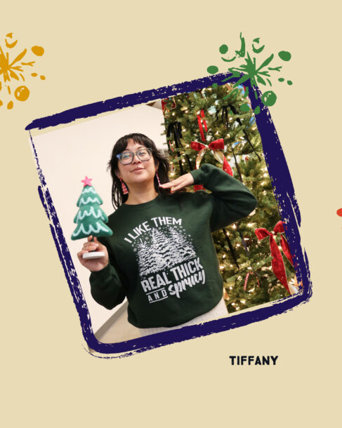 SiteCrafting employee Tiffany holding a small plush tree. She is wearing a green sweatshirt with tree illustrations that reads, 
