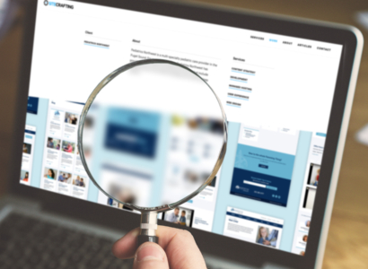 A bearded man holding a magnifying glass in front of a laptop screen.