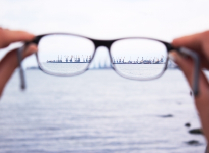 Hands holding out a pair of glasses in front of a body of water.