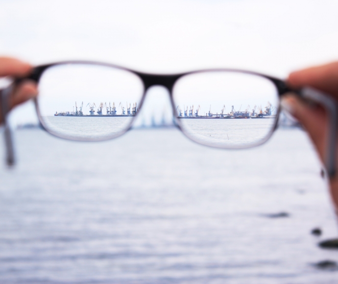 Hands holding out a pair of glasses in front of a body of water.