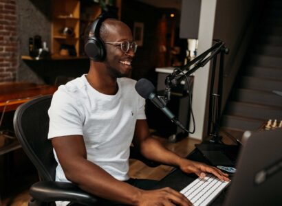 African American man sitting at a computer wearing headphones and talking into a microphone.