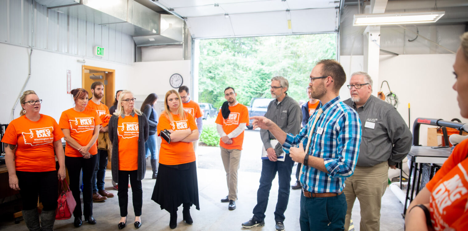 A group of men and woman listening to instructions from a man in a warehouse.