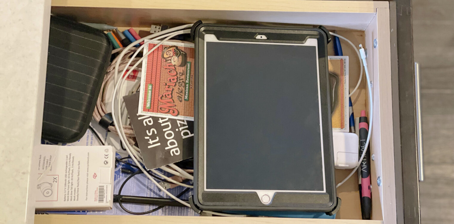 Junk drawer filled with cluttered cords, papers and electronics.