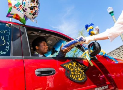 Graduate in car receiving a package through the car window.