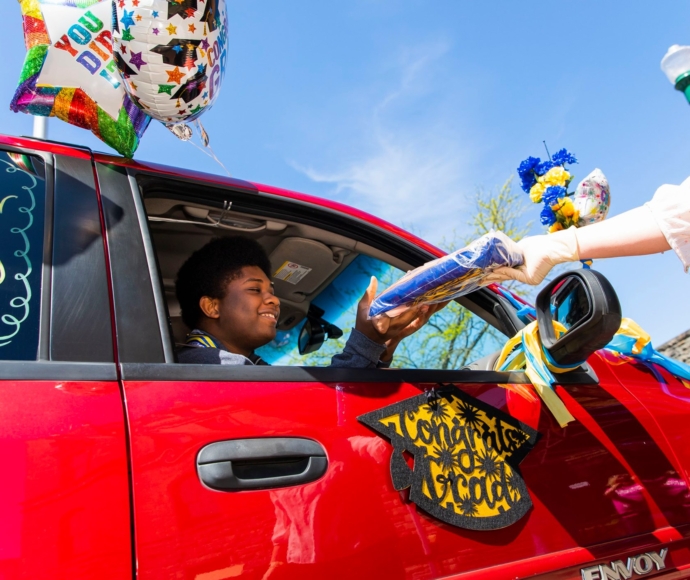 Graduate in car receiving a package through the car window.