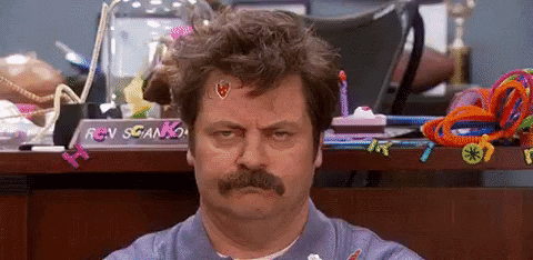 An upset dad with stickers on his face sitting on the floor of a messy room while his children play around him