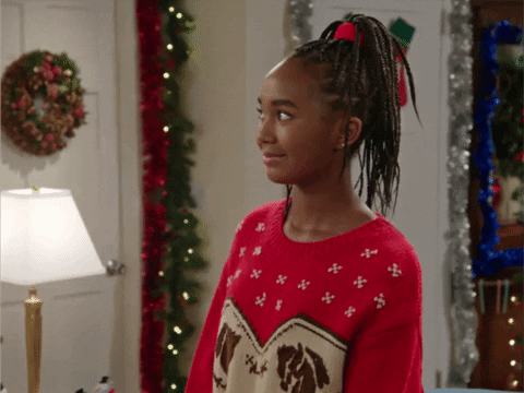 A girl standing in a Christmas-decorated room, smiling disapprovingly