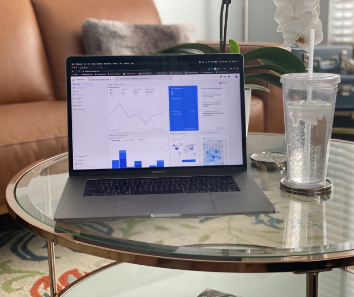 Laptop showing with the google analytics dashboard open while sitting on a coffee table next to a glass of water.