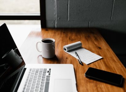 Laptop, coffee, phone and notepad sitting on a desk.