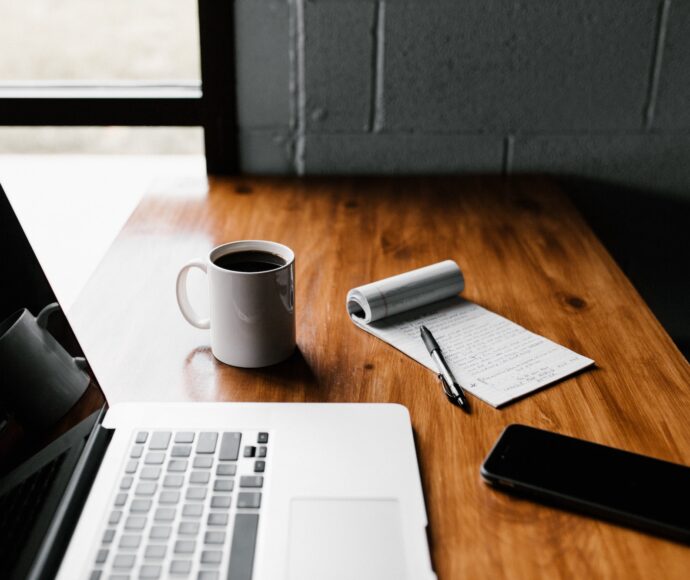 Laptop, coffee, phone and notepad sitting on a desk.