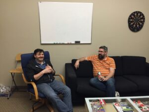 Ken Foubert sitting in a chair next to Mike Ash  sitting on a couch in an office (taken in 2014)