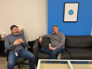 Ken Foubert sitting in a chair next to Mike Ash sitting on a couch in an office (taken in 2020)