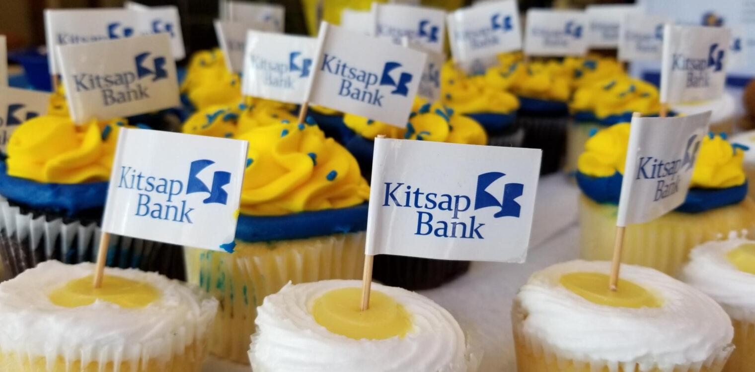 Blue, white and yellow frosting on cupcakes decorated with sprinkles and Kitsap Bank logo flags.