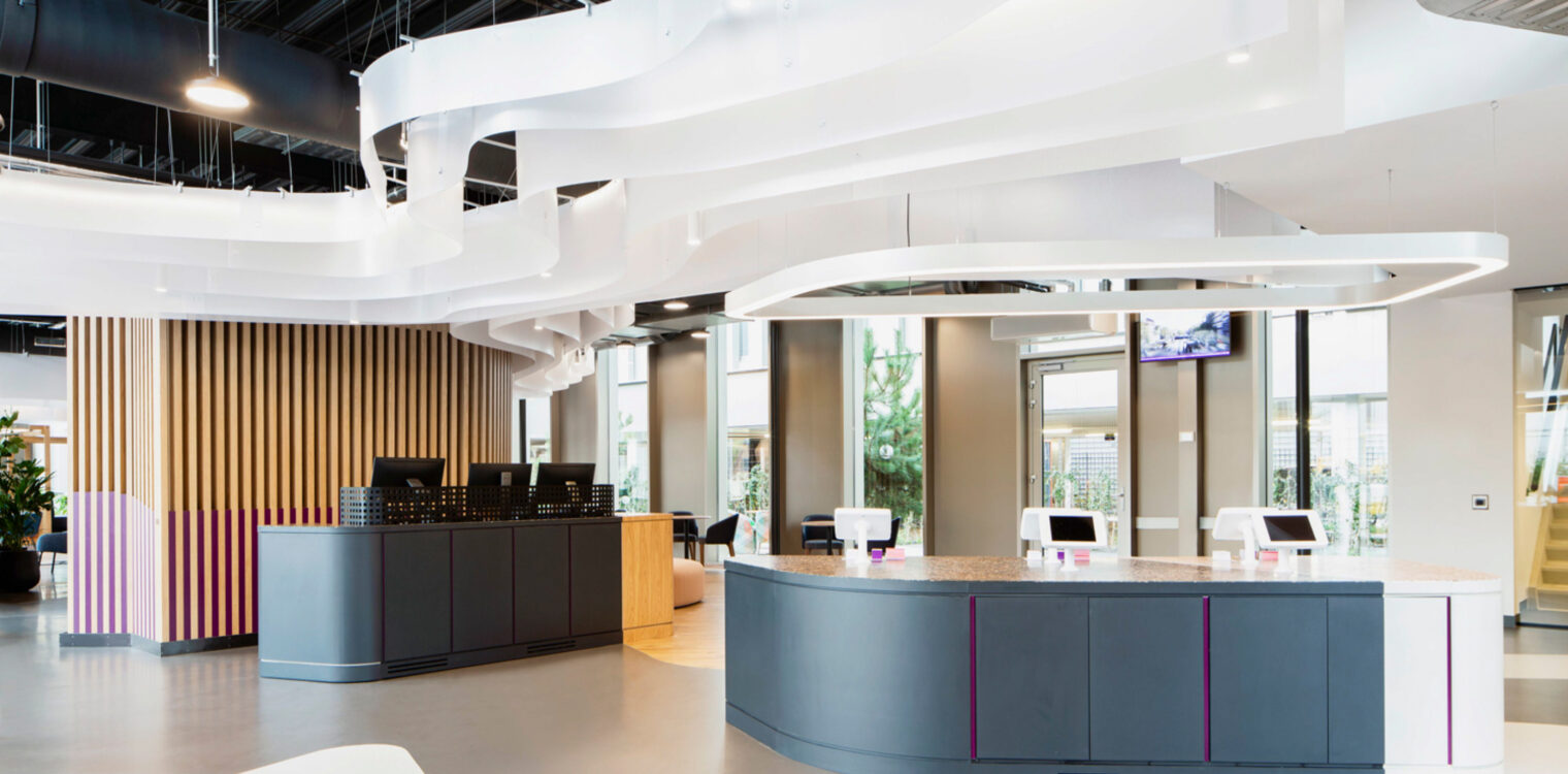 Modern reception area with a curved desk featuring multiple computer terminals, wave-like ceiling installations, large windows providing natural light, and seating areas. Wooden wall slats and clean-lined furniture create a professional, welcoming atmosphere.