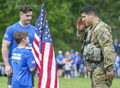 Military soldier saluting a child holding an American flag.