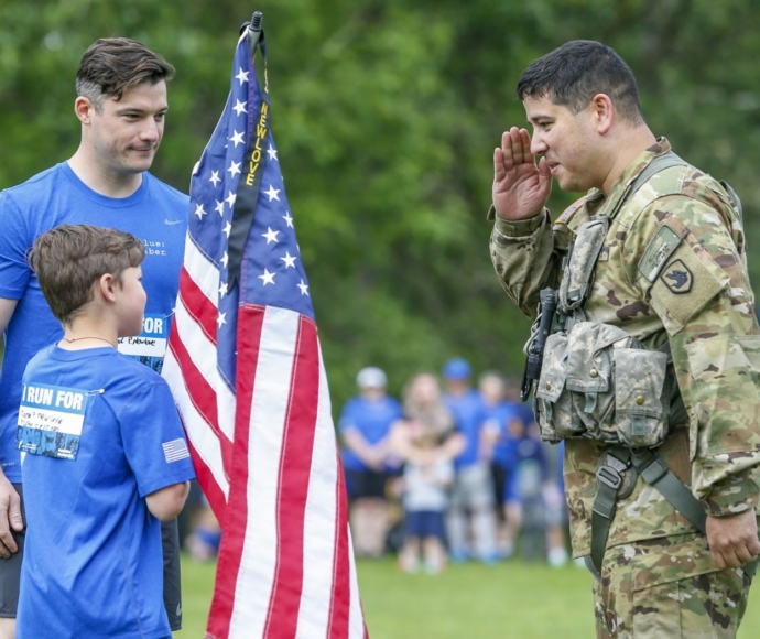 Military soldier saluting a child holding an American flag.
