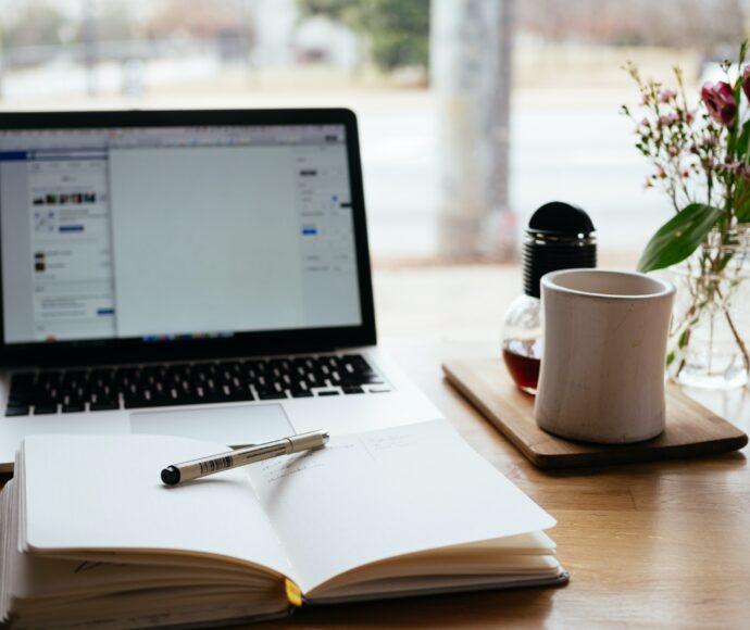 Blank notebook on a desk in front of an open laptop
