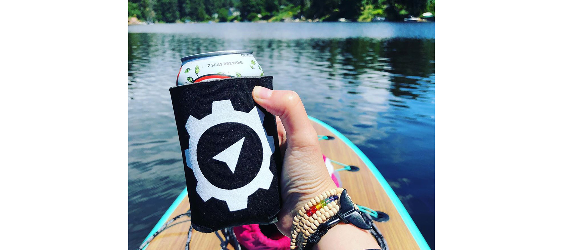 Hand holding a beer in a SiteCrafting koosie while on a lake.