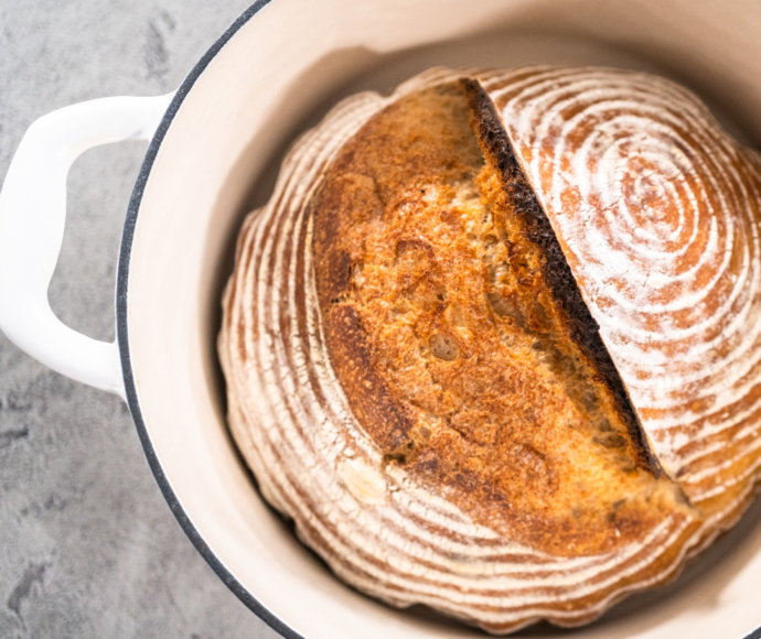 Freshly baked loaf of a wheat sourdough bread with marks from bread proofing basket in enameled cast iron dutch oven.
