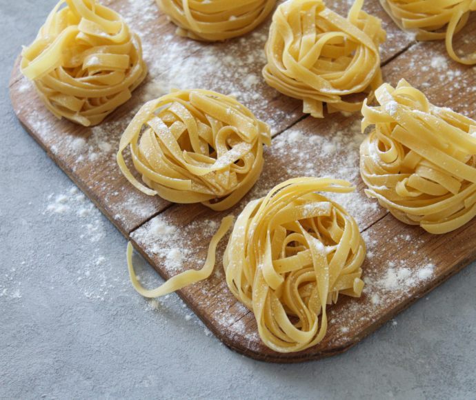 Raw fresh homemade pasta tagliatelle with flour on wooden board close-up and side view