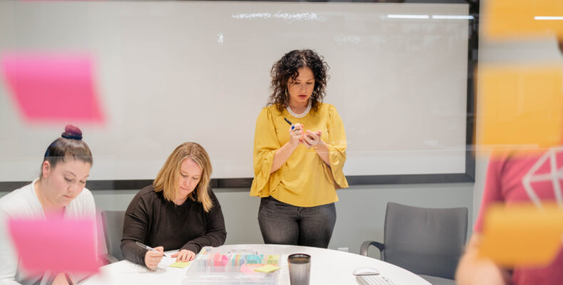 Jen Rittenhouse, Crissy Paguylan and other SiteCrafting team members write on post-it notes during a meeting.