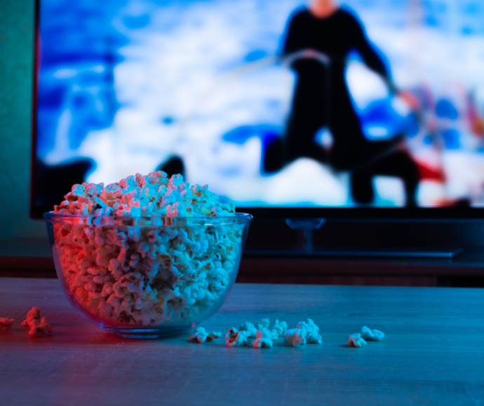 Bowl of popcorn sitting on a table in front of a TV playing a show