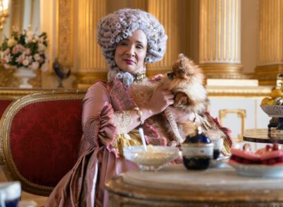 Woman sitting at a table of treats dressed in 16th century royalty fashion holding a Pomeranian.