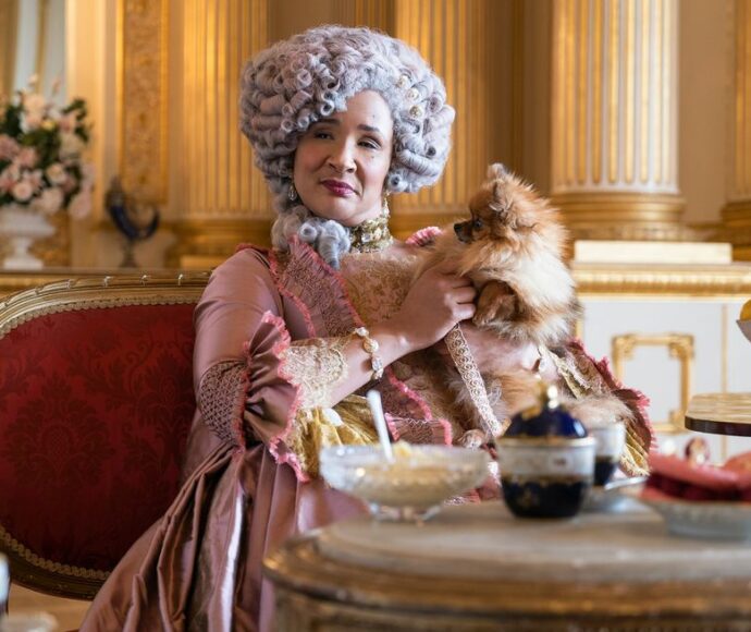 Woman sitting at a table of treats dressed in 16th century royalty fashion holding a Pomeranian.